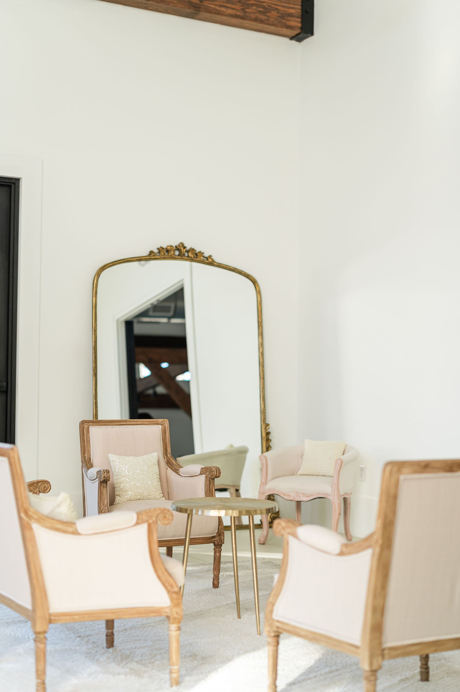 Room with four light-colored armchairs around a small table, large ornate mirror reflects the room.