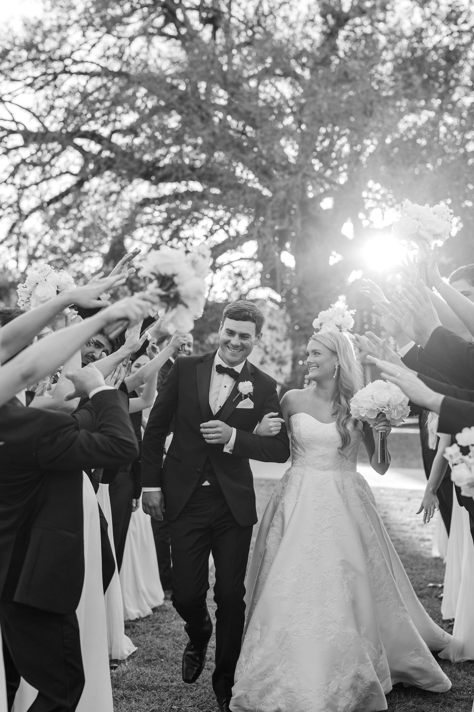 Newly married couple walking through raised bouquets, smiling. Outdoor wedding. Black and white.