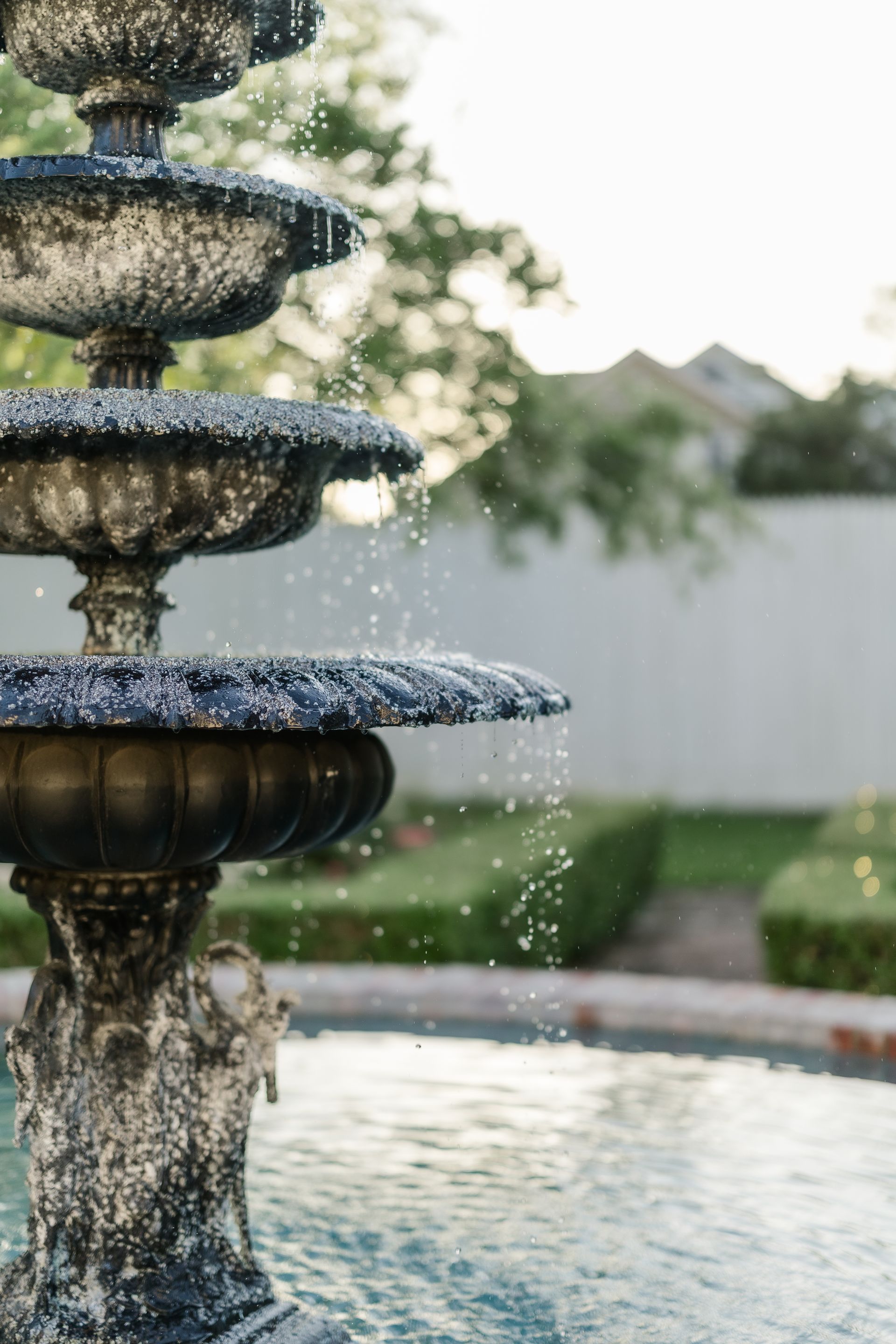 Stone tiered fountain with water droplets, in a garden setting.