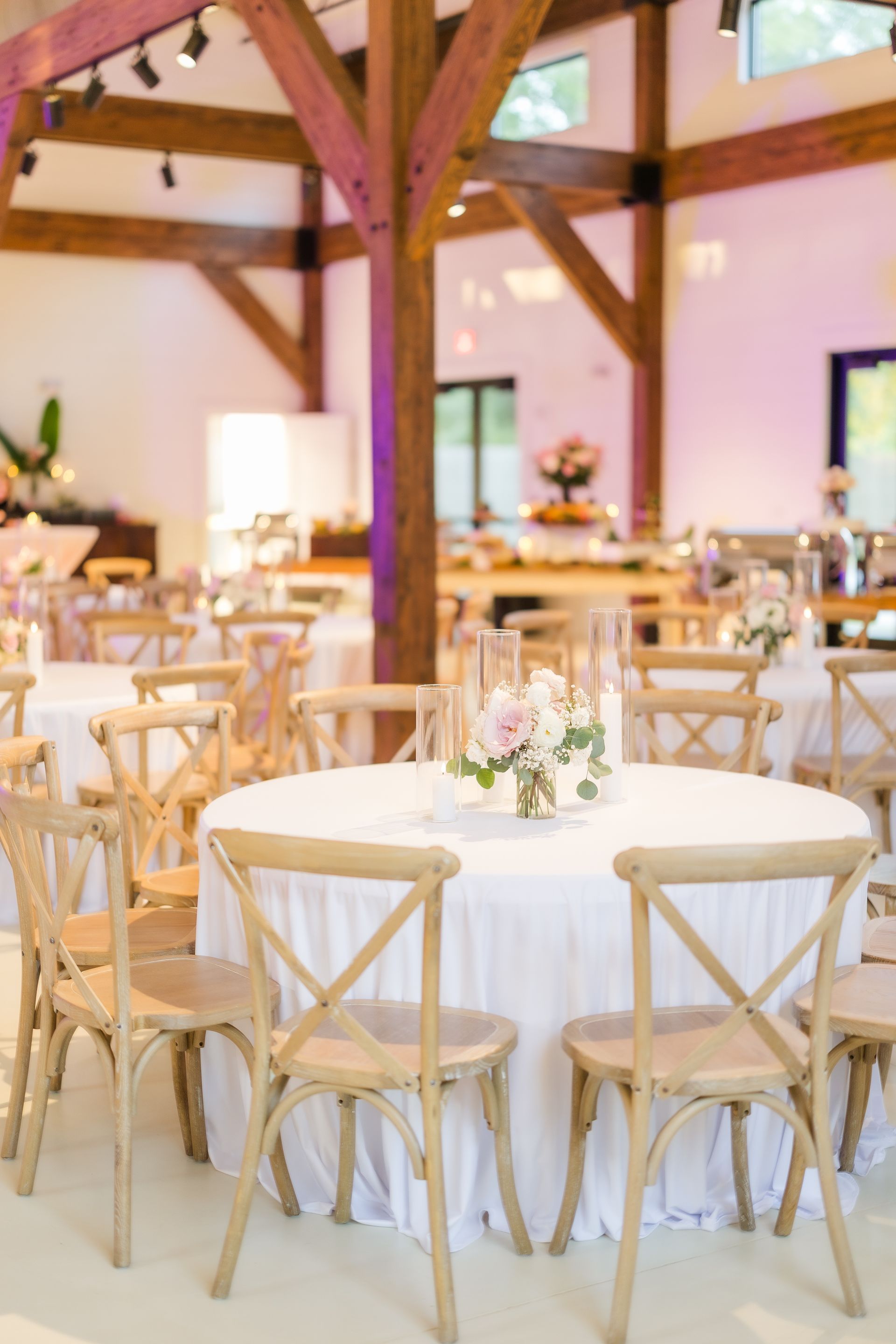 Wedding reception venue with round tables, white linens, wooden chairs, and floral centerpieces.