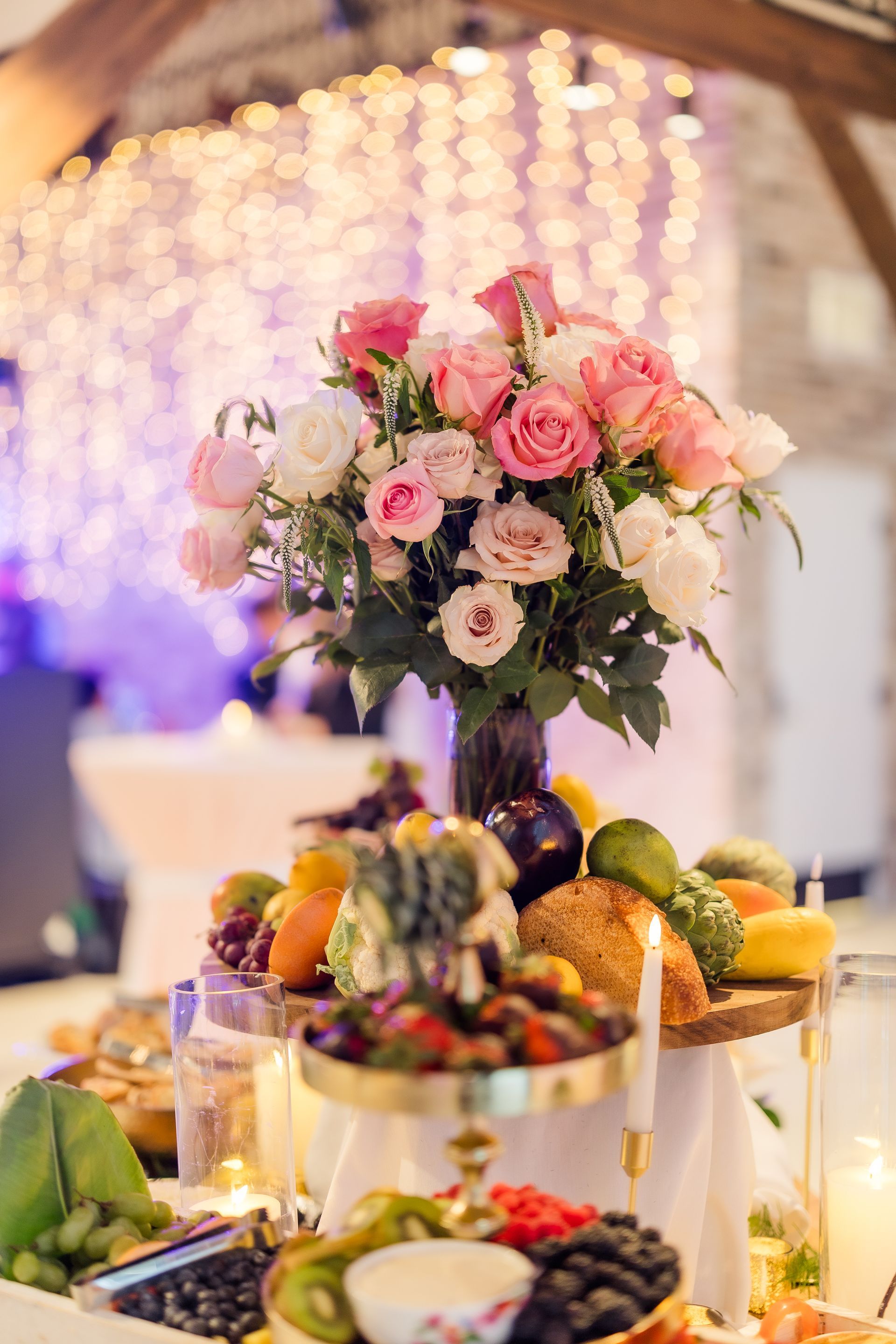 Floral centerpiece on a fruit and vegetable display; soft pink, white roses.