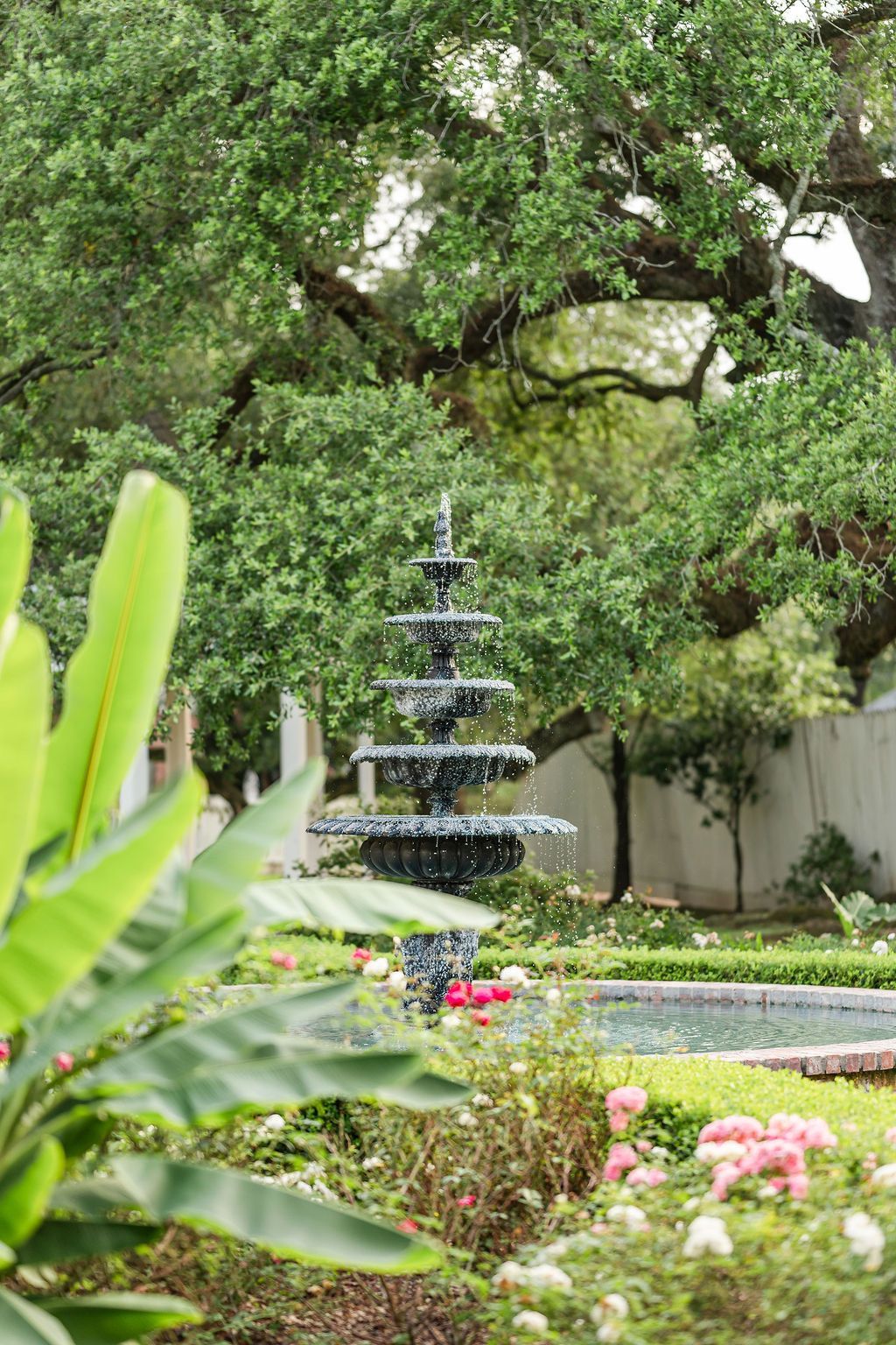 A tiered fountain in a lush garden, surrounded by trees and flowers.