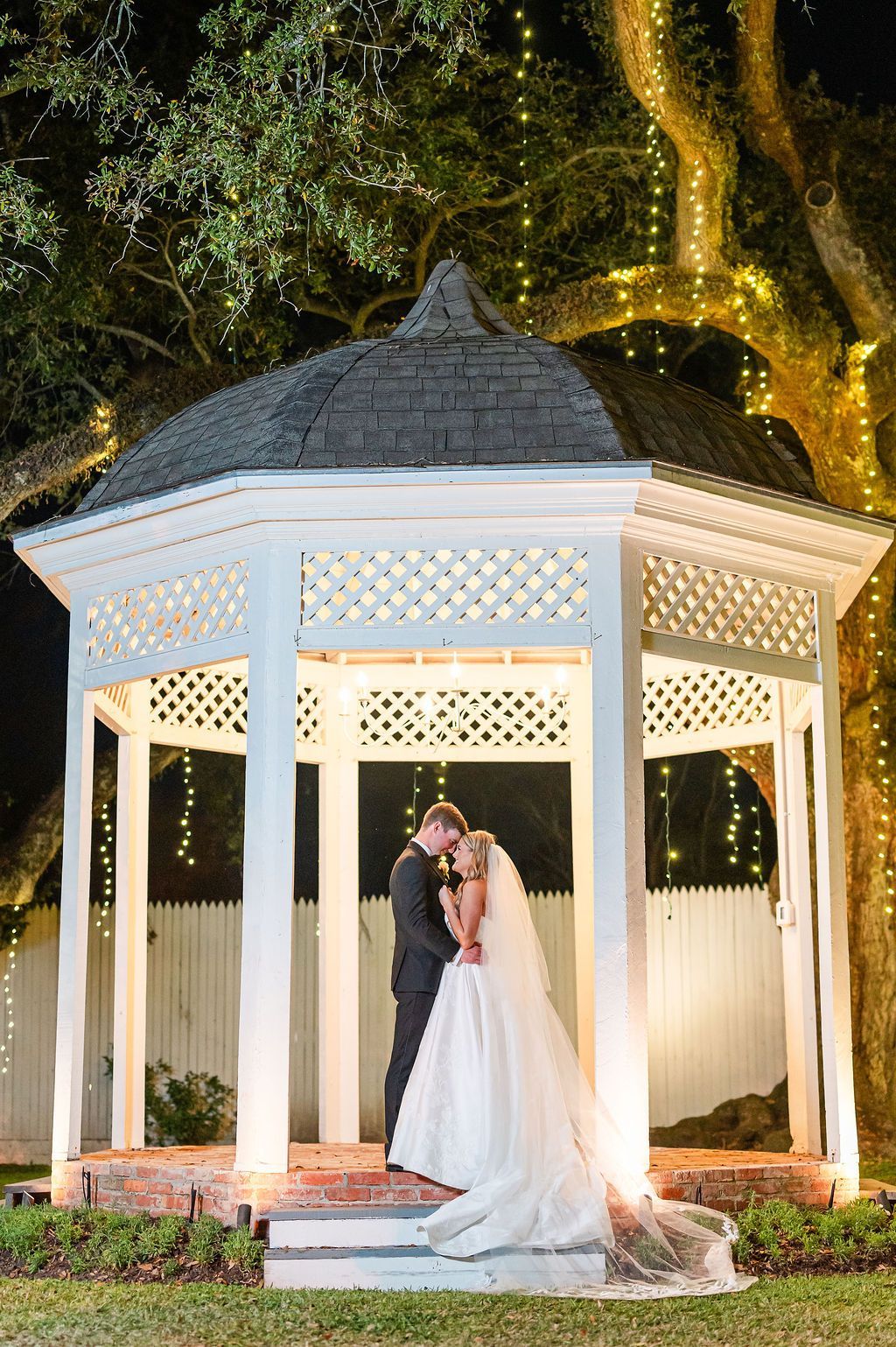 Couple embraces inside a gazebo at night, lit by string lights.