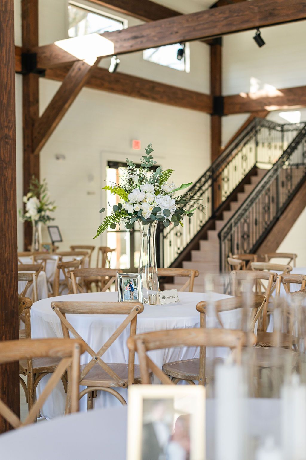 Wedding reception with tables, floral centerpieces, wooden chairs, and a staircase.