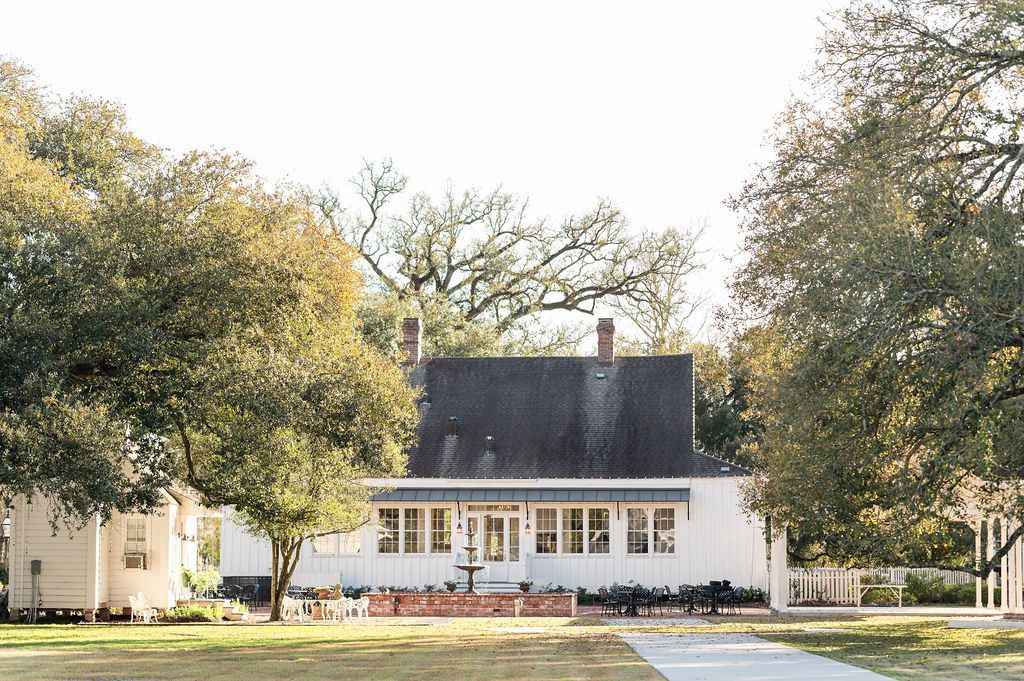 White building with a dark roof and large windows framed by trees on a sunny day.