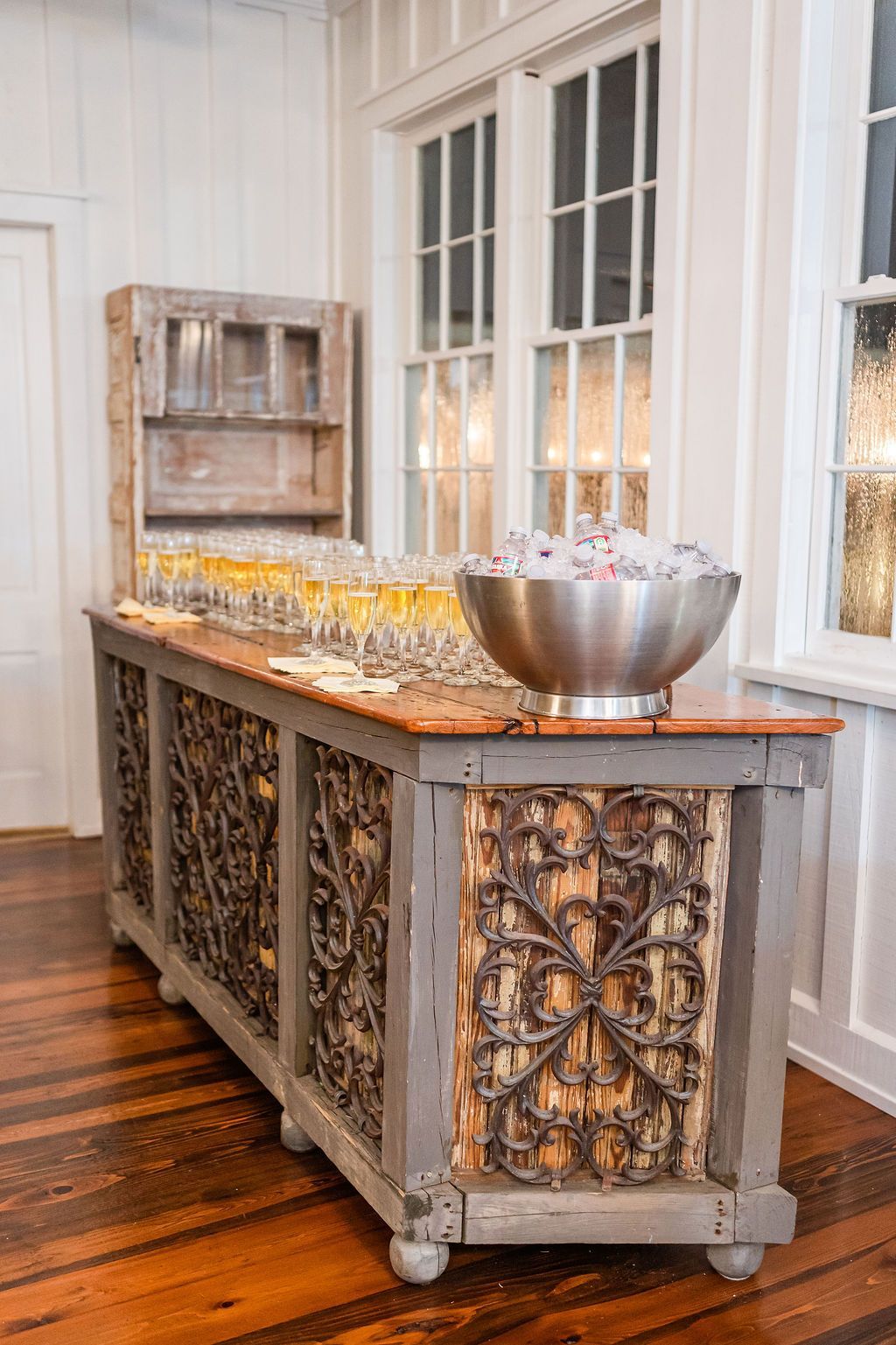 Rustic wooden bar with decorative metal panels, drinks, and ice bucket near windows.
