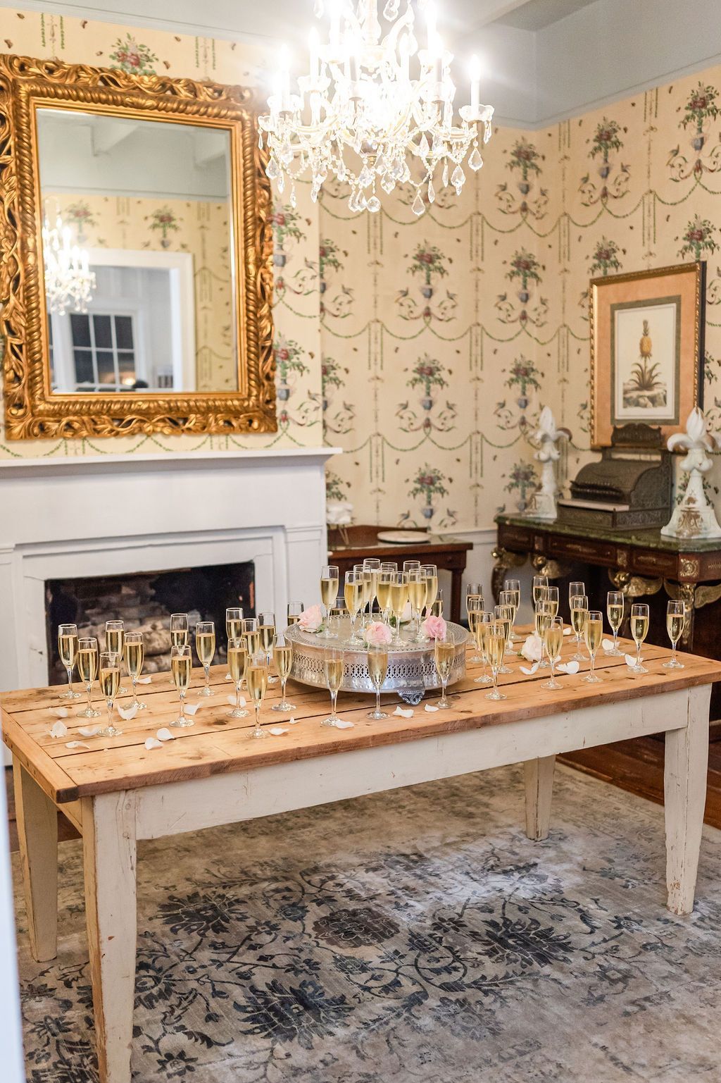 Room set for a celebration: table with champagne flutes, fireplace, ornate mirror, and chandelier.
