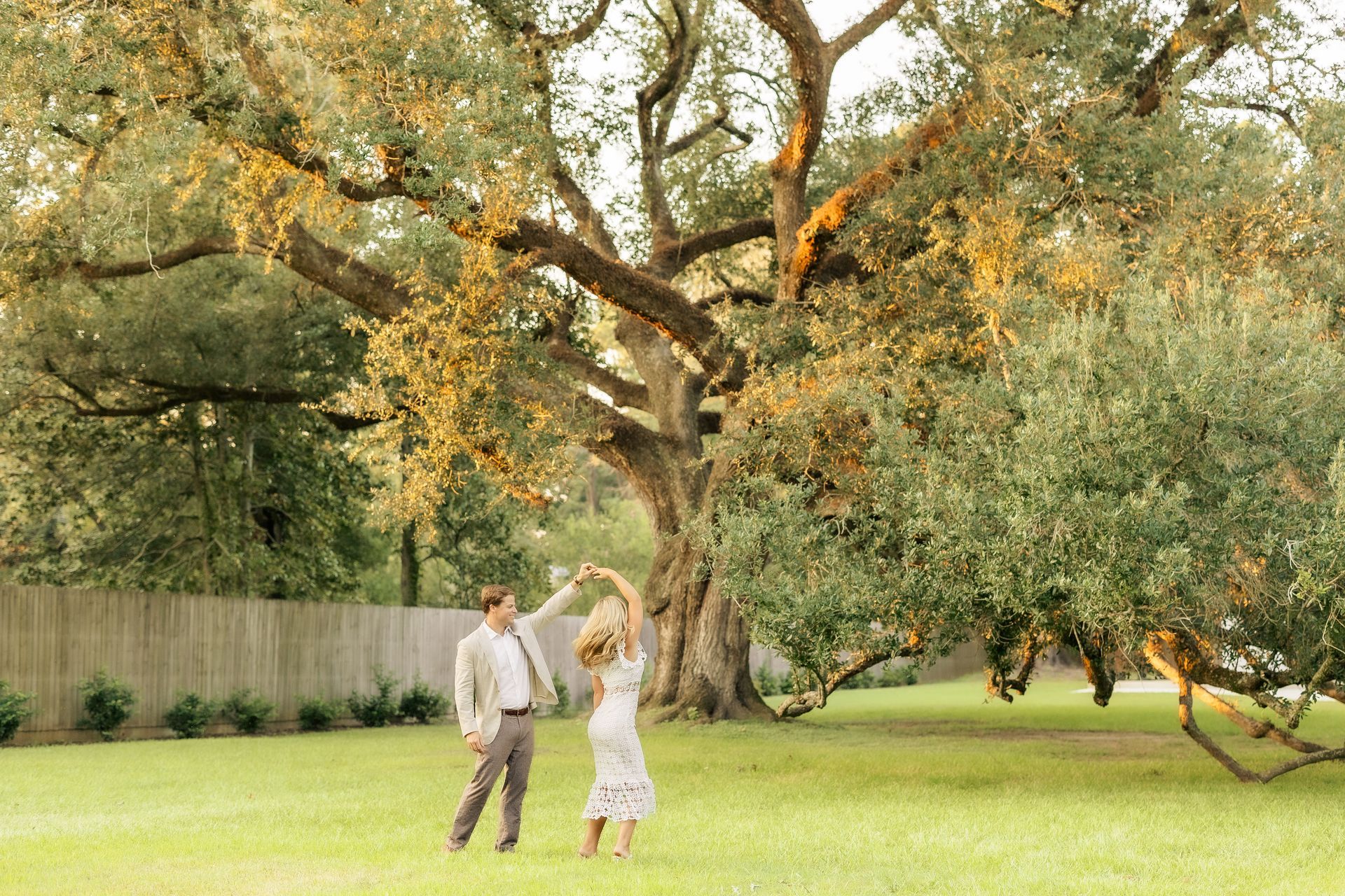 Couple dancing under a large tree in a grassy yard; sunny golden light.