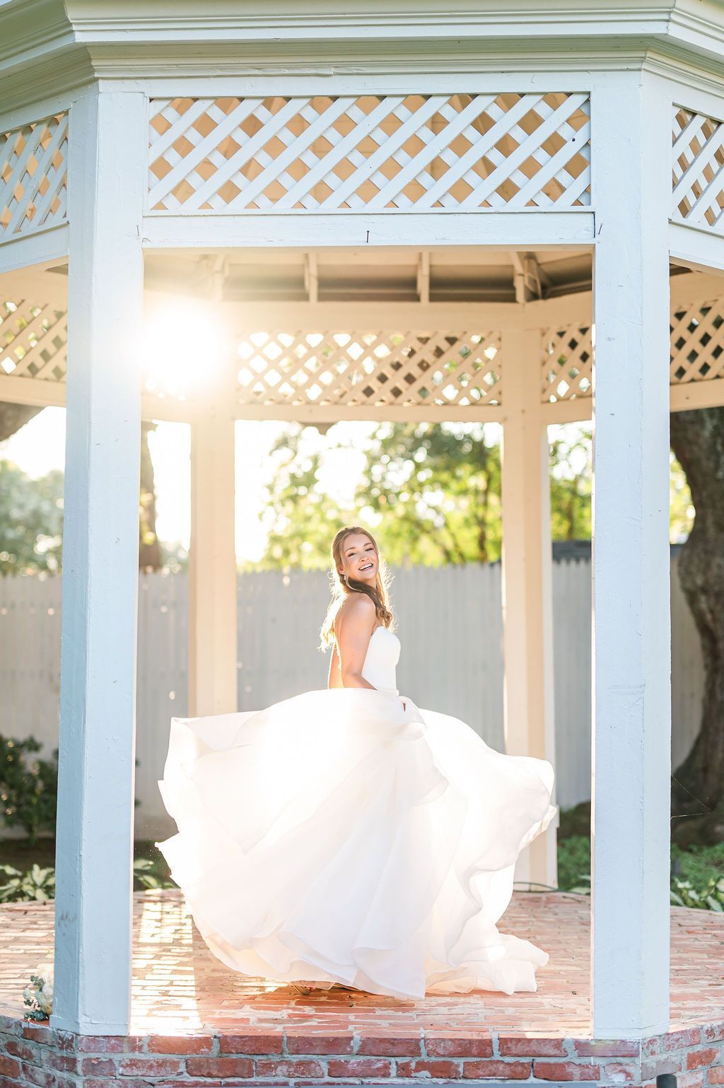 Bride twirling in wedding dress inside a gazebo, sunlight behind her.