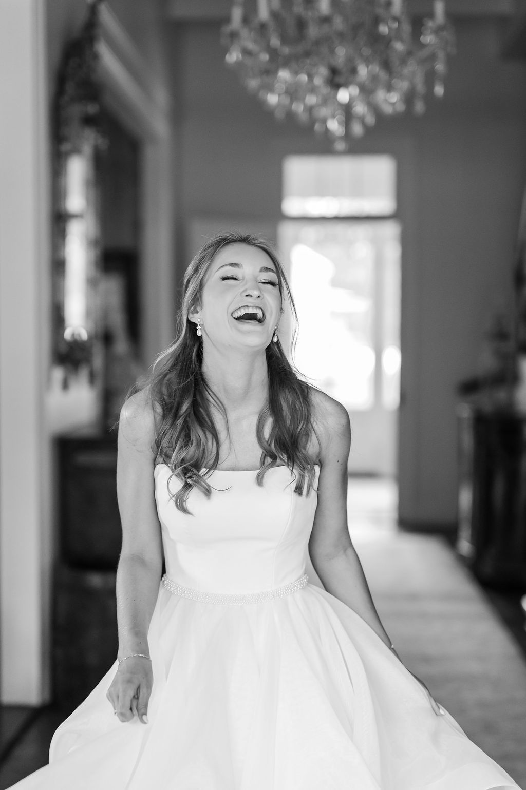 Woman in a white wedding dress laughs in a hallway with a chandelier.