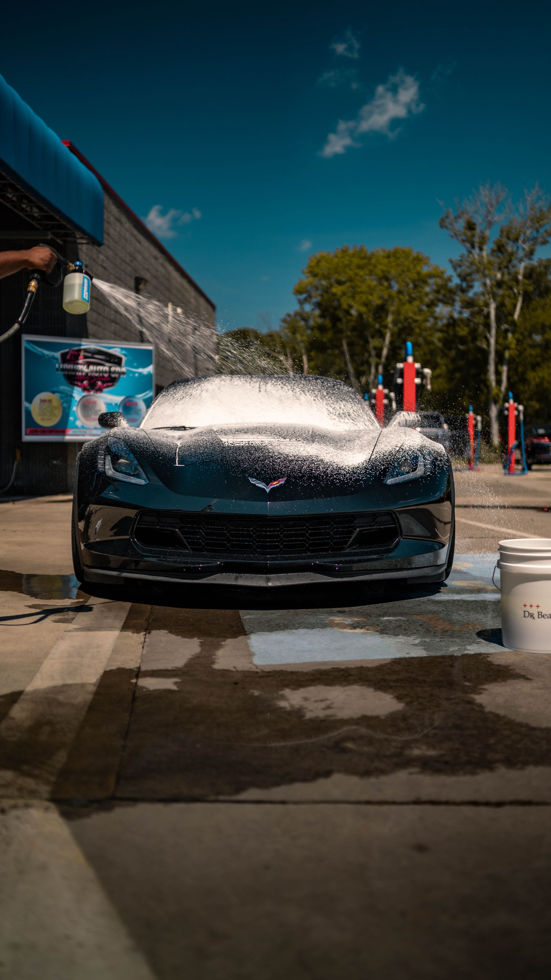 A blue corvette is being washed with foam at a car wash.