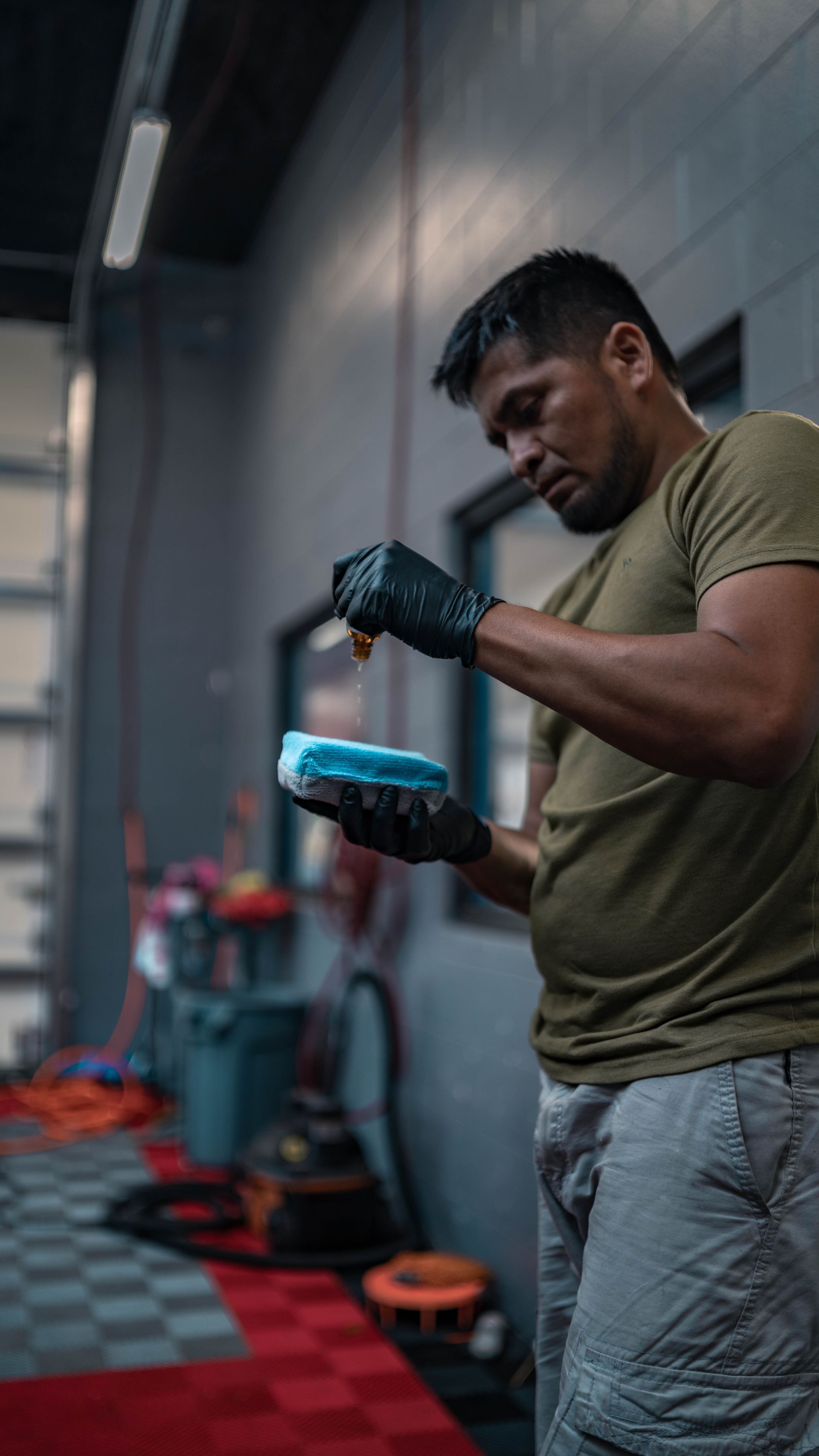 A man is cleaning a car with a sponge in a garage.