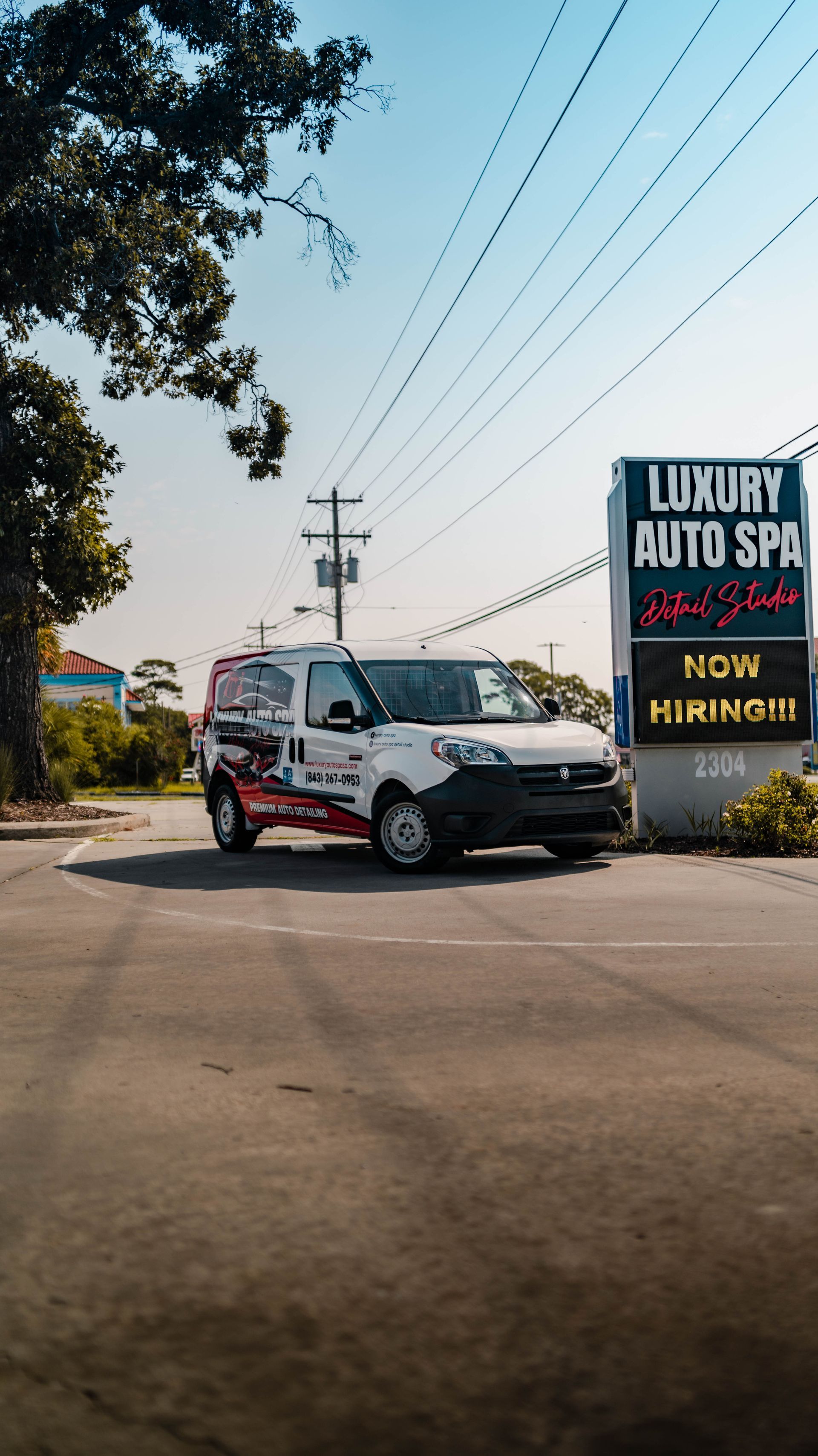A white van is parked in front of a sign for luxury auto spa.