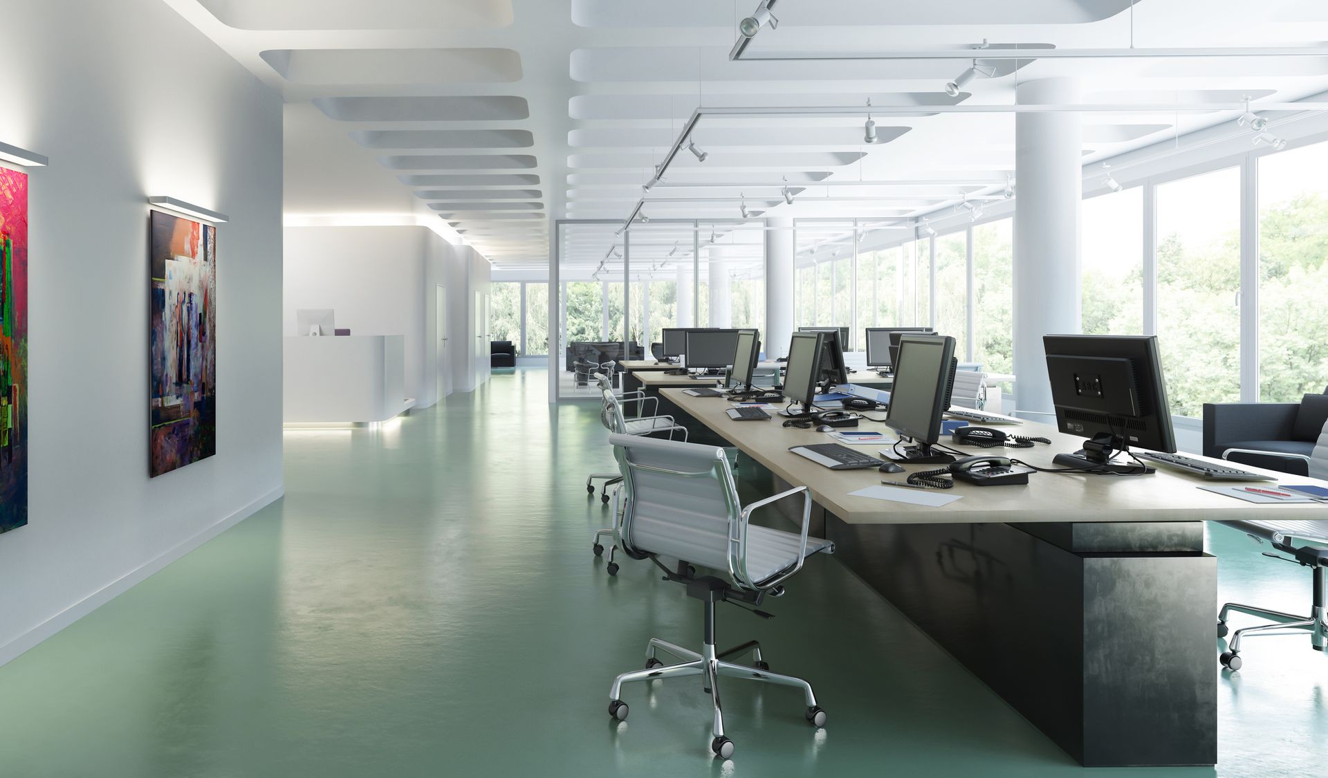 Modern office interior with long desks, computer screens, chairs, and artwork on the wall.
