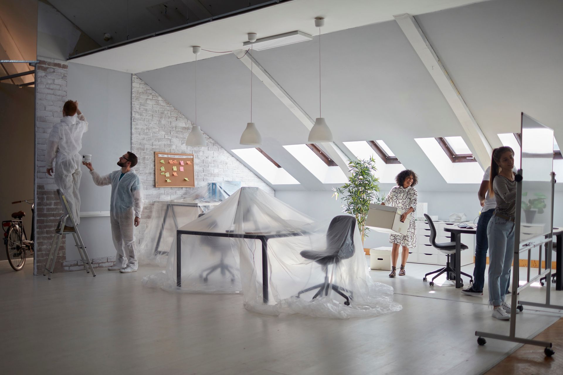 People renovating an office: painting walls, covering furniture, moving boxes, and adjusting dividers.