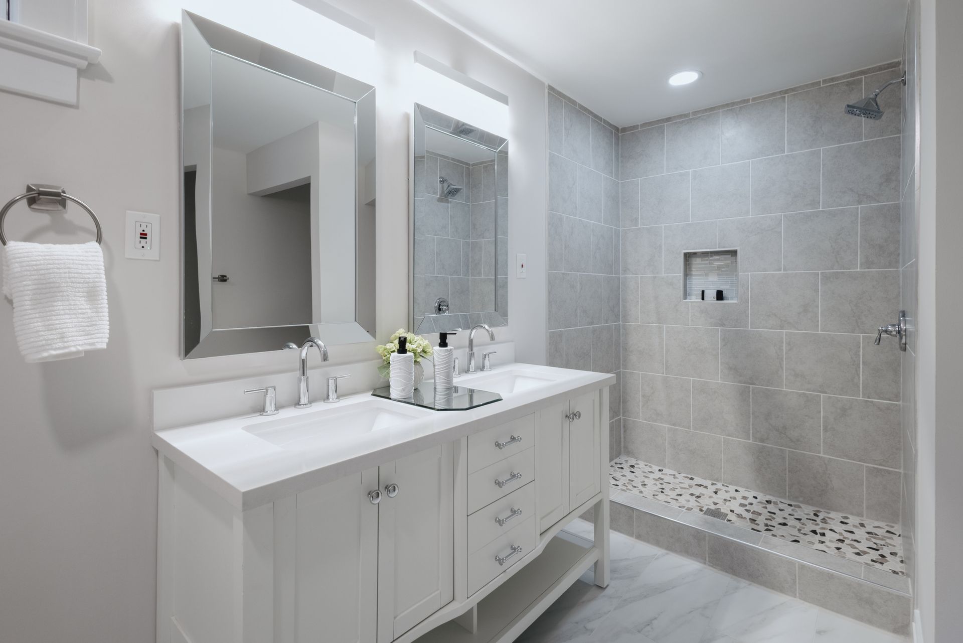 Modern bathroom with double sinks, large mirrors, and a tiled shower. White and gray tones.