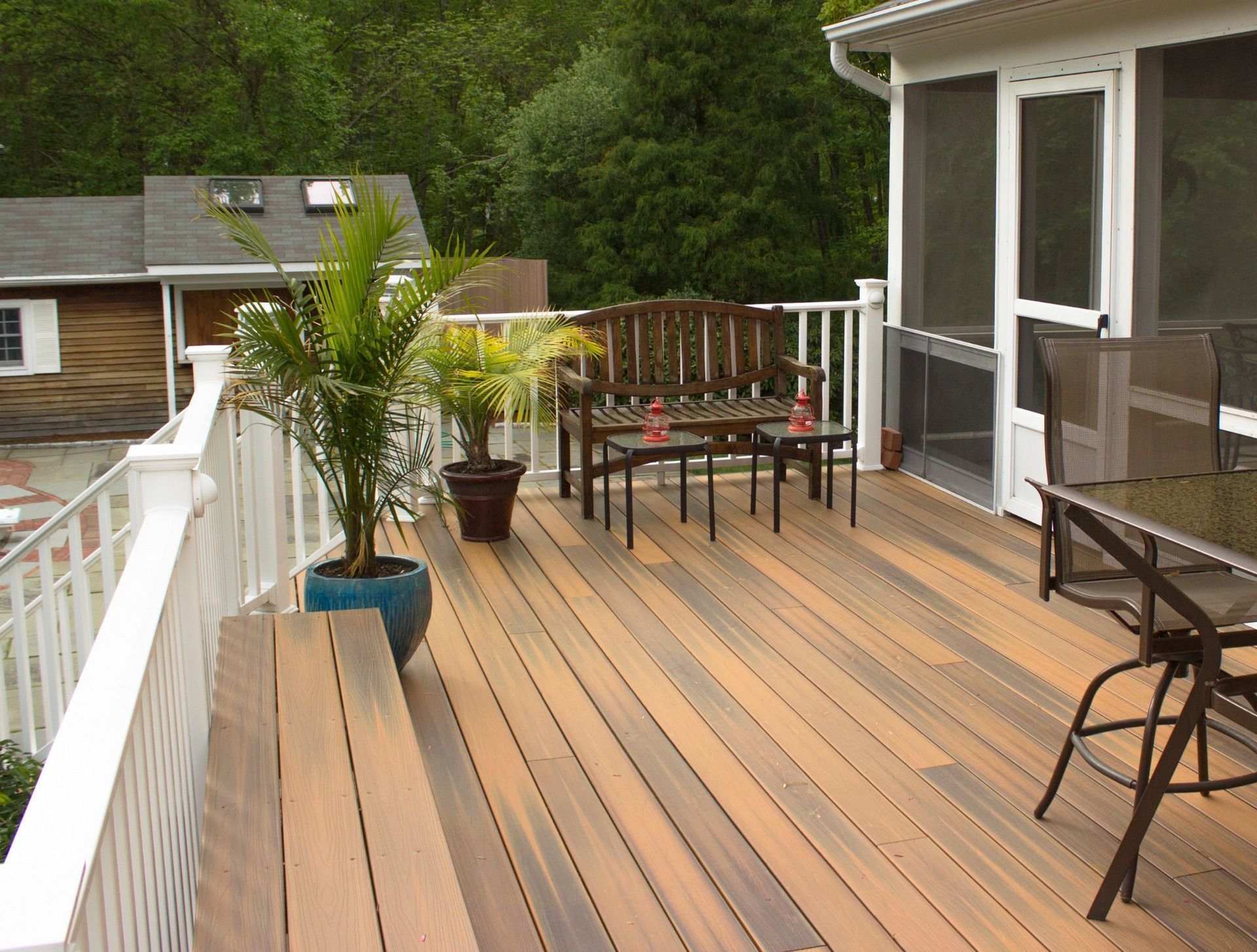 Backyard deck with wicker furniture, orange pillow, brick and stone, green lawn, trees.