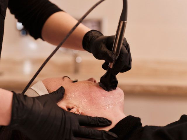 Donna che scrive alla scrivania, sorridente, di fronte a un'altra donna in un ambiente professionale con un computer portatile e dei documenti.