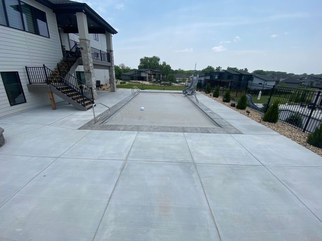 Concrete patio with a covered pool next to a two-story house with black metal railings.