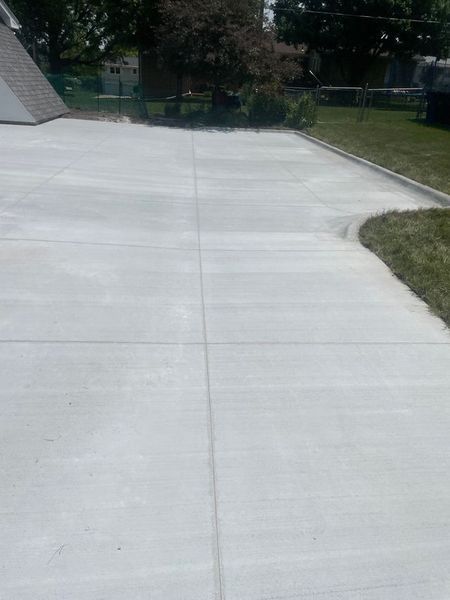 Newly poured concrete driveway with grid lines, next to green grass.