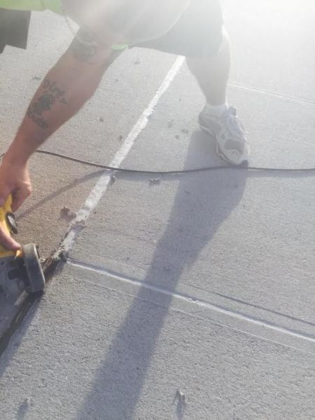 Person using a power saw to cut a line in a concrete surface. The person is wearing shorts and sneakers.