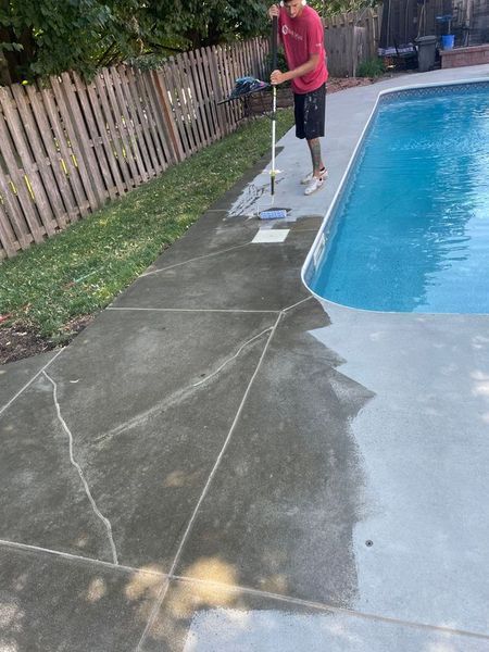 Person spraying concrete around a swimming pool. The concrete has cracks.