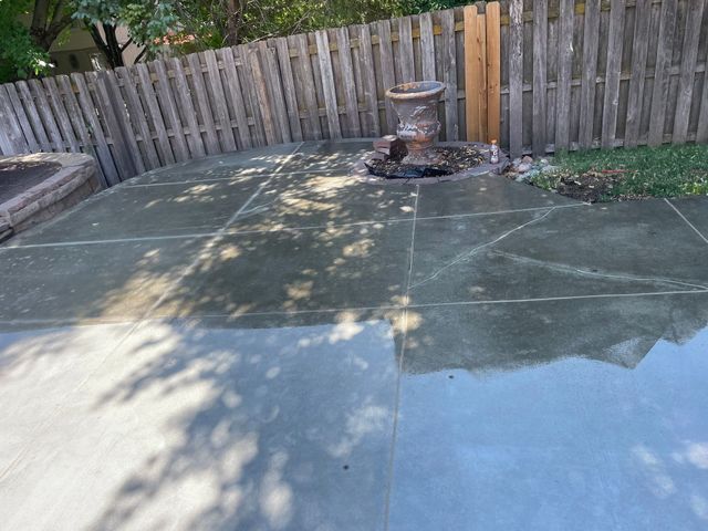 Wet concrete patio with a fence and a decorative stone feature.