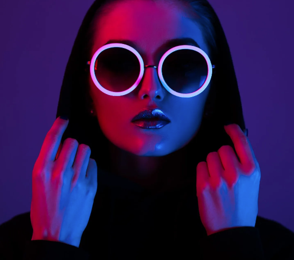 A woman wearing sunglasses and a hoodie is glowing in the dark.