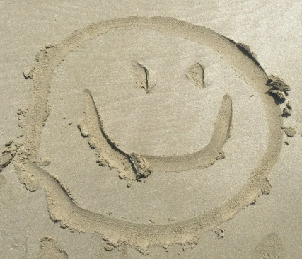 A smiley face is drawn in the sand on the beach