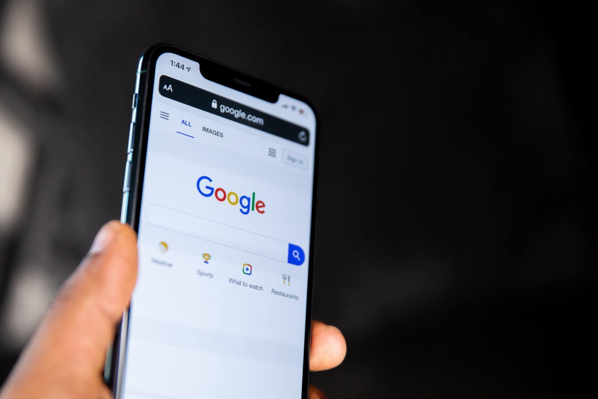 A person is holding a cell phone with the google search page open.