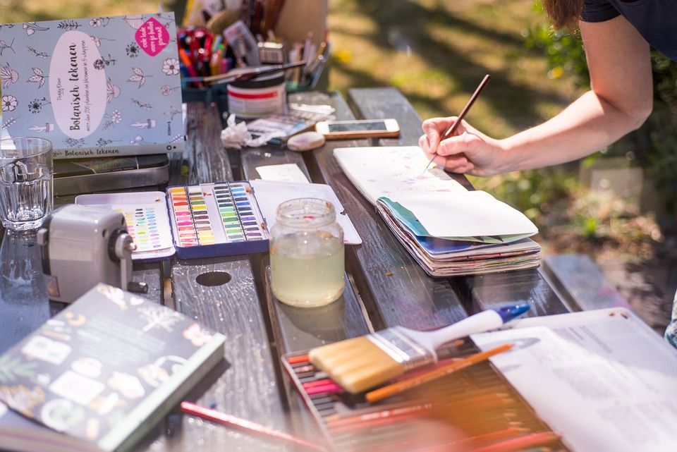 a woman's hand painting in a watercolor journal
