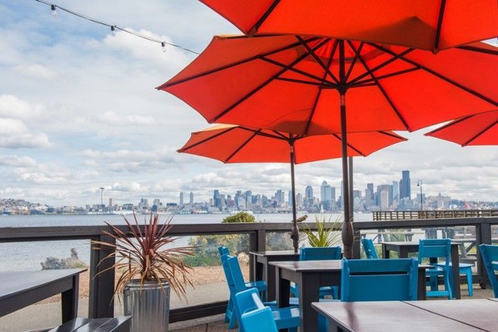 The view of the Seattle city skyline from Marination Ma Kai in West Seattle, with orange umbrellas in the forground. 