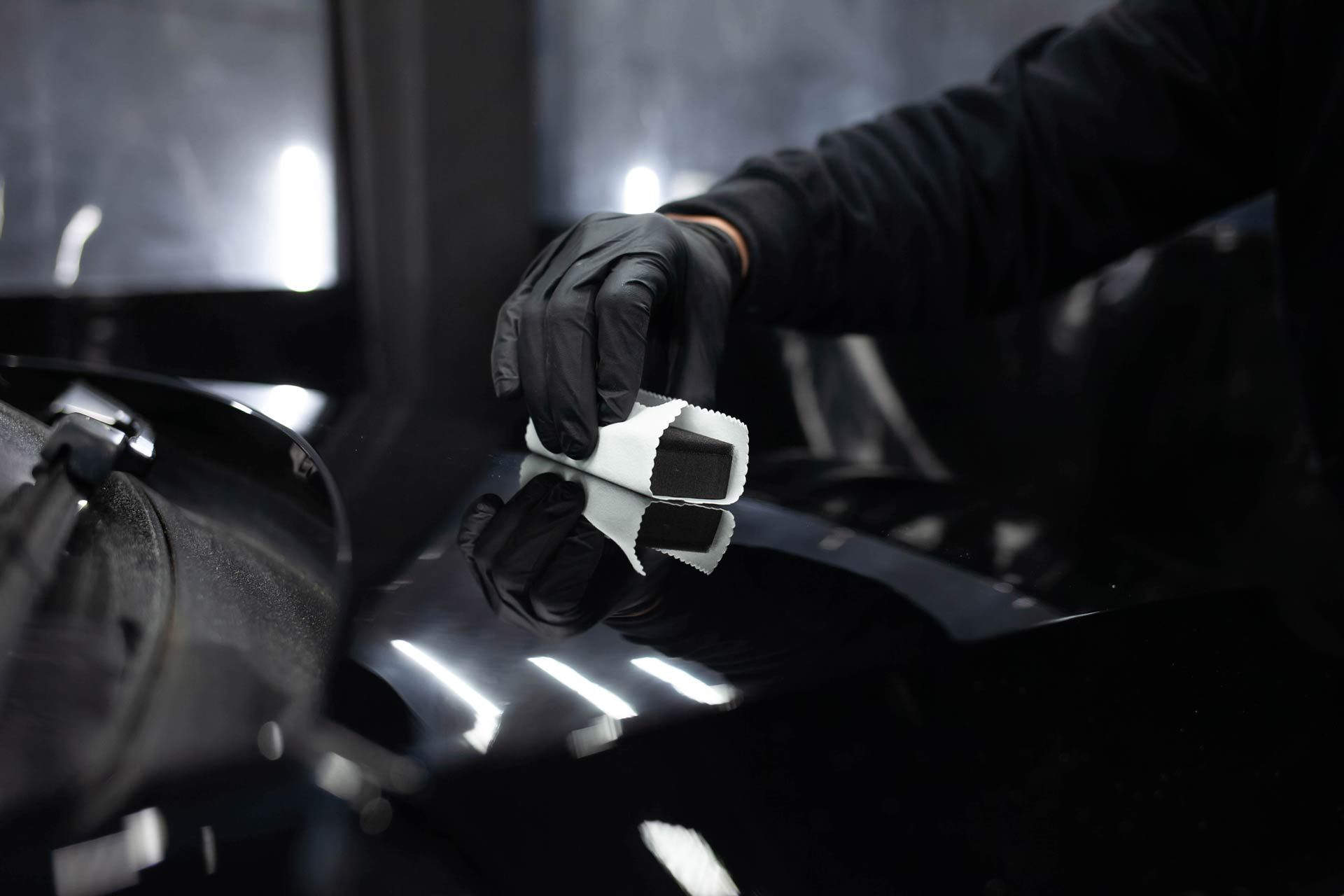 A person wearing black gloves is polishing a car hood.