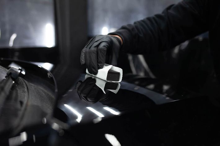 A person wearing black gloves is polishing a car hood.