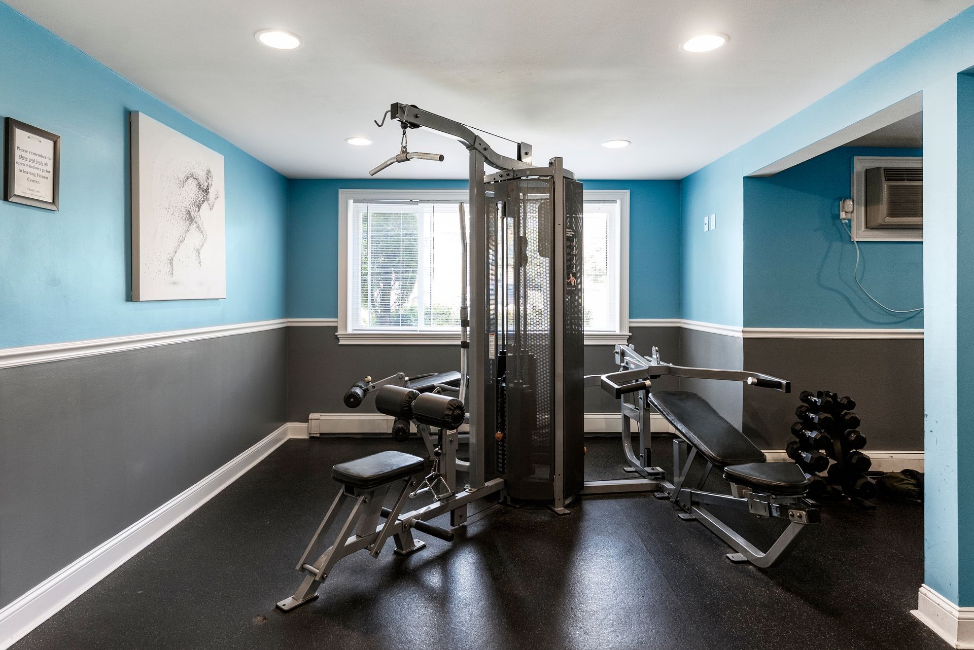 Home gym with blue and gray walls, weight machine, weights, and adjustable bench at The Groves at Milford in Milford, MA.