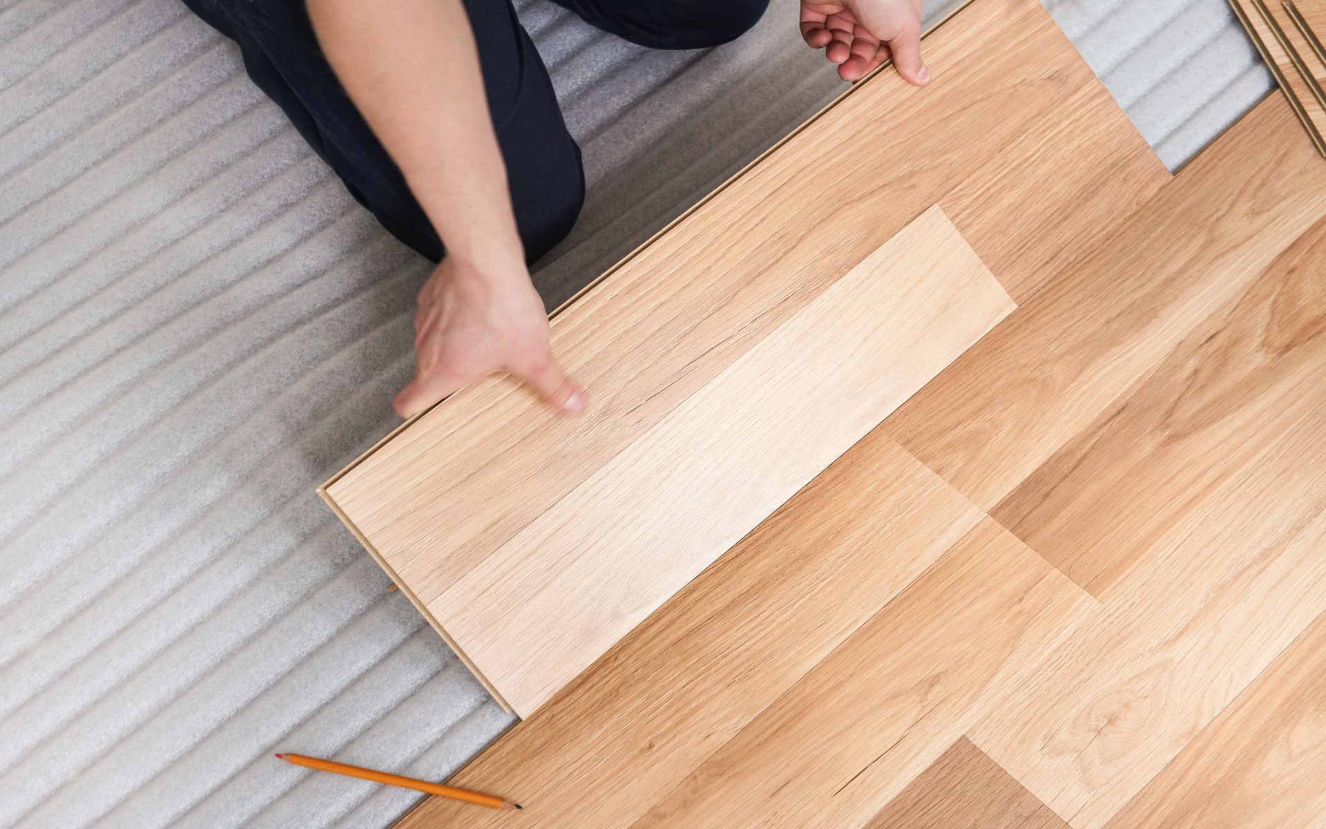 Person installing wood flooring, holding a plank over a partially completed floor.