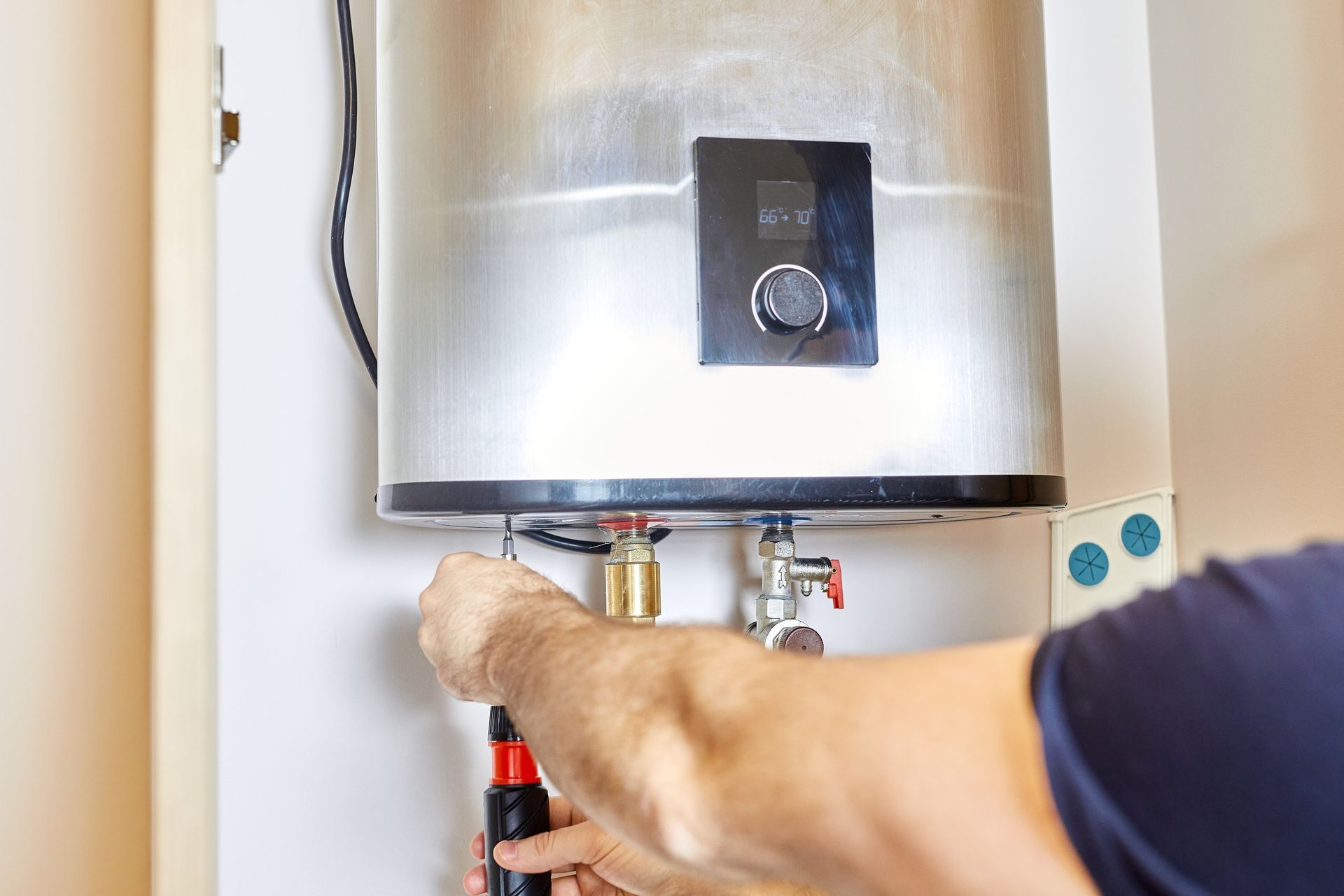 Person using a screwdriver to work on a stainless steel water heater in a utility closet.