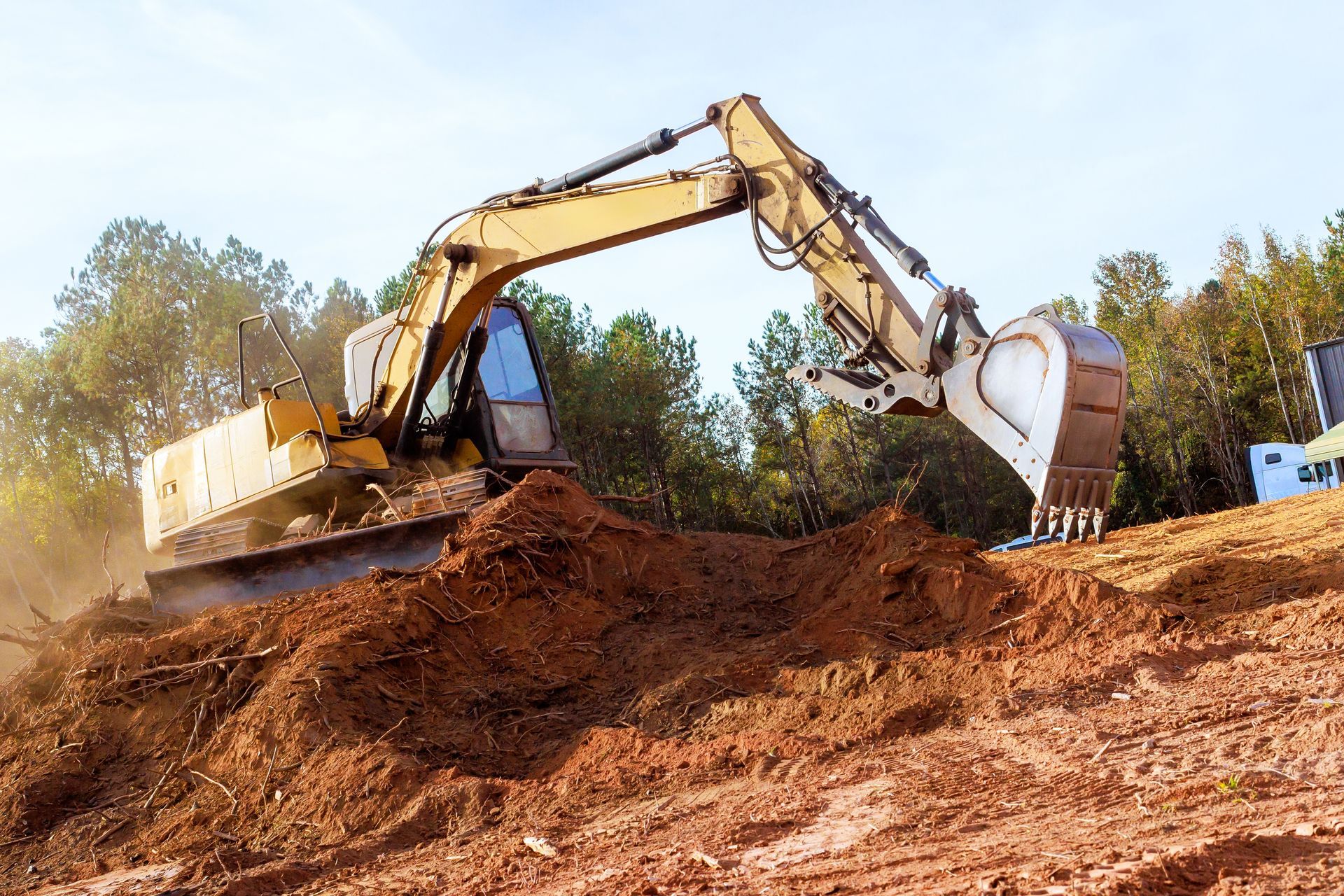 Yellow excavator digging into a pile of red dirt outdoors.