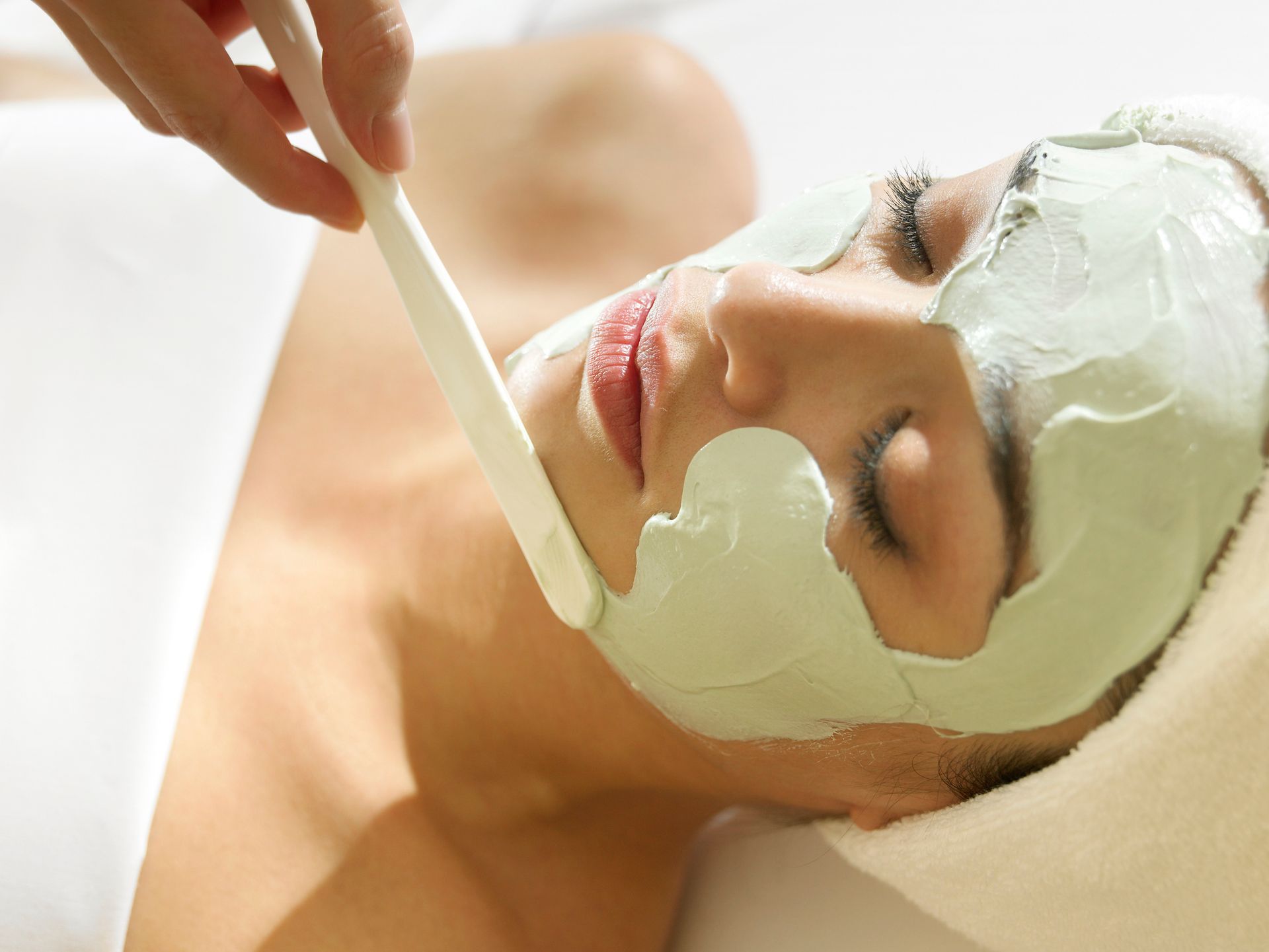 Una donna si sta sottoponendo a un trattamento per il viso con una maschera verde sul viso.