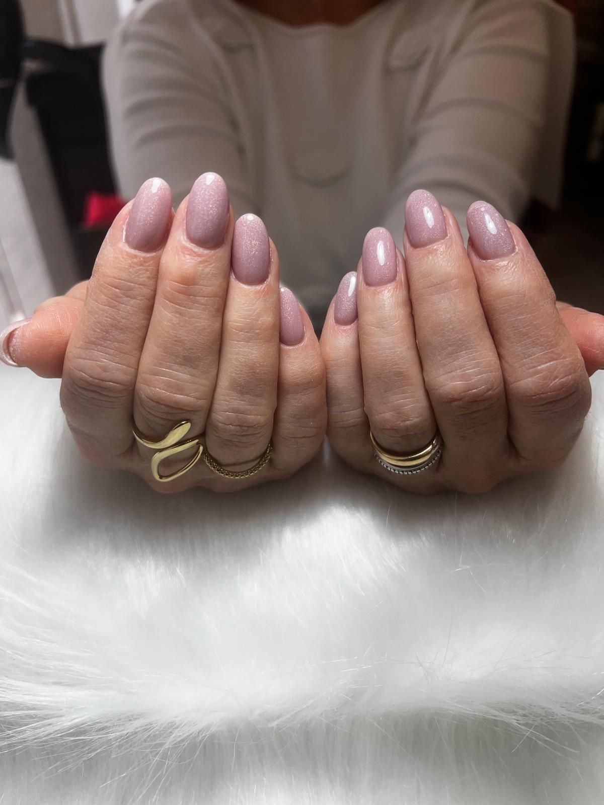 Un primo piano delle mani di una donna con unghie e anelli rosa.