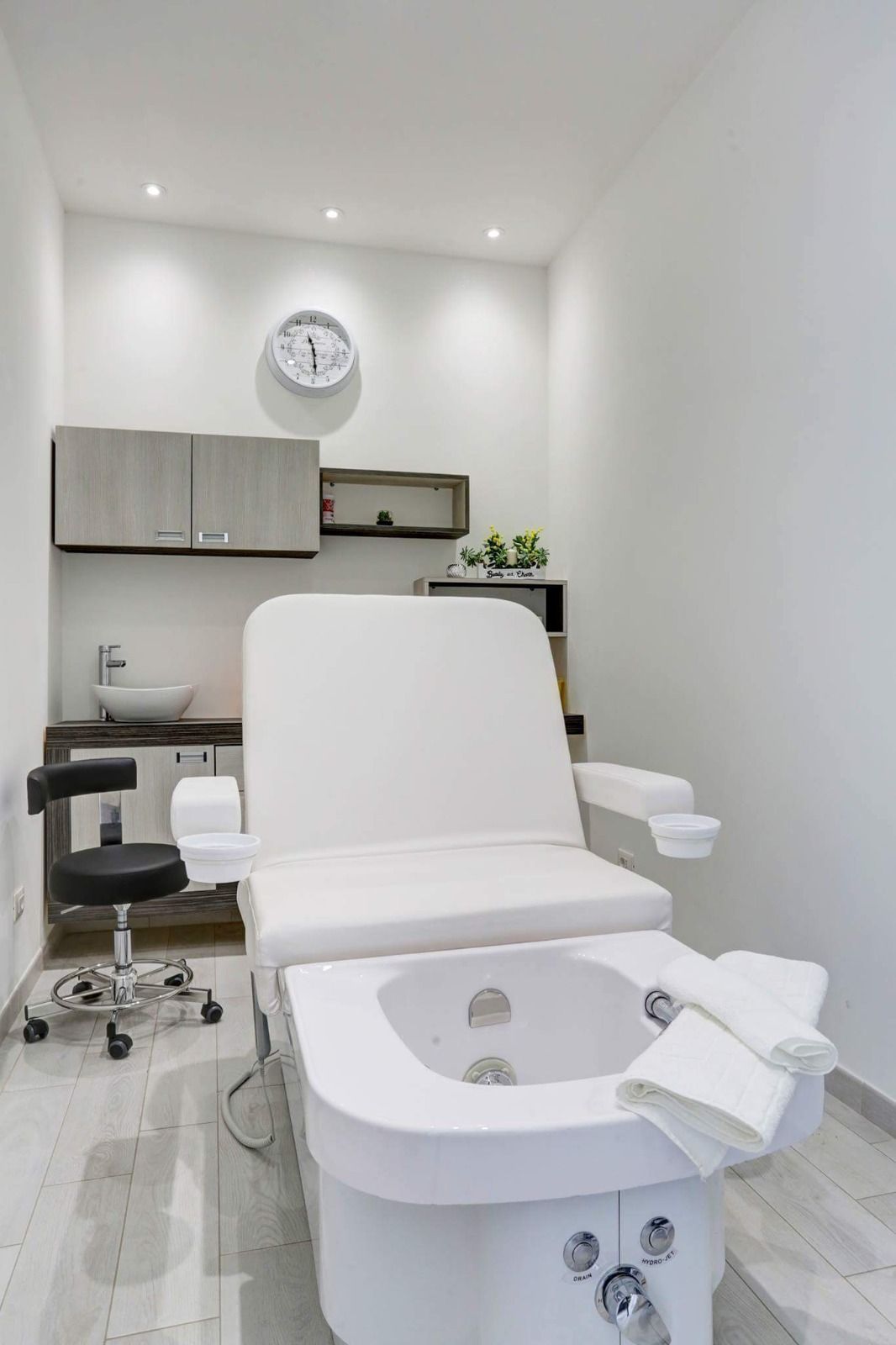 Una sedia bianca con una vaschetta per i piedi in una stanza con un orologio sul muro.