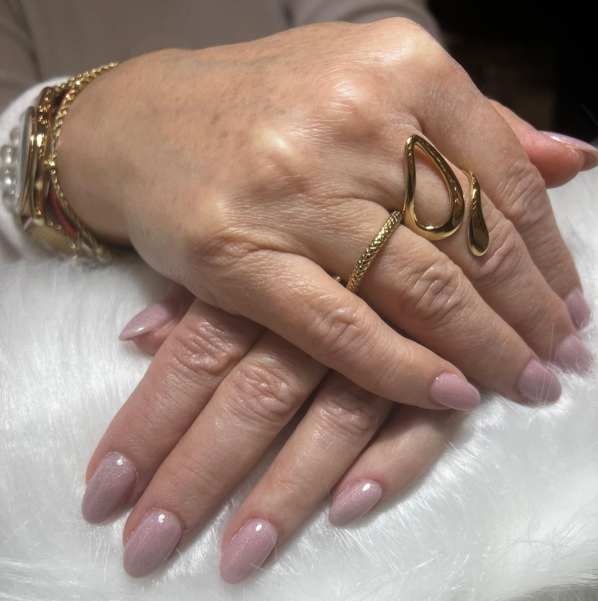 La mano di una donna con le unghie rosa e un anello d'oro