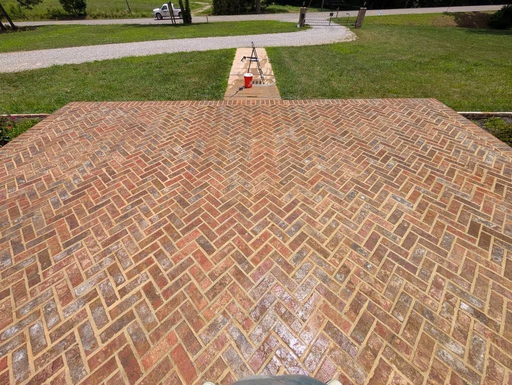 Brick patio in a herringbone pattern, outdoors. Green grass, a white vehicle, and pathway are in the background.
