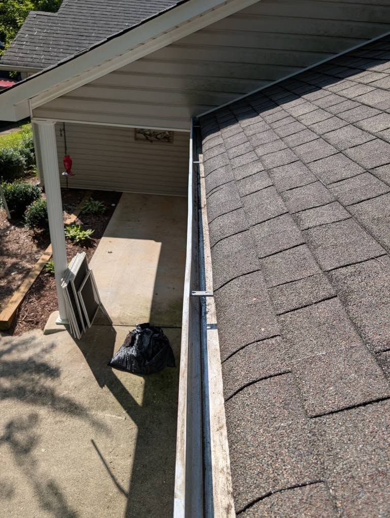 Gutter along a roof edge next to a porch with gray shingles and concrete walkway.
