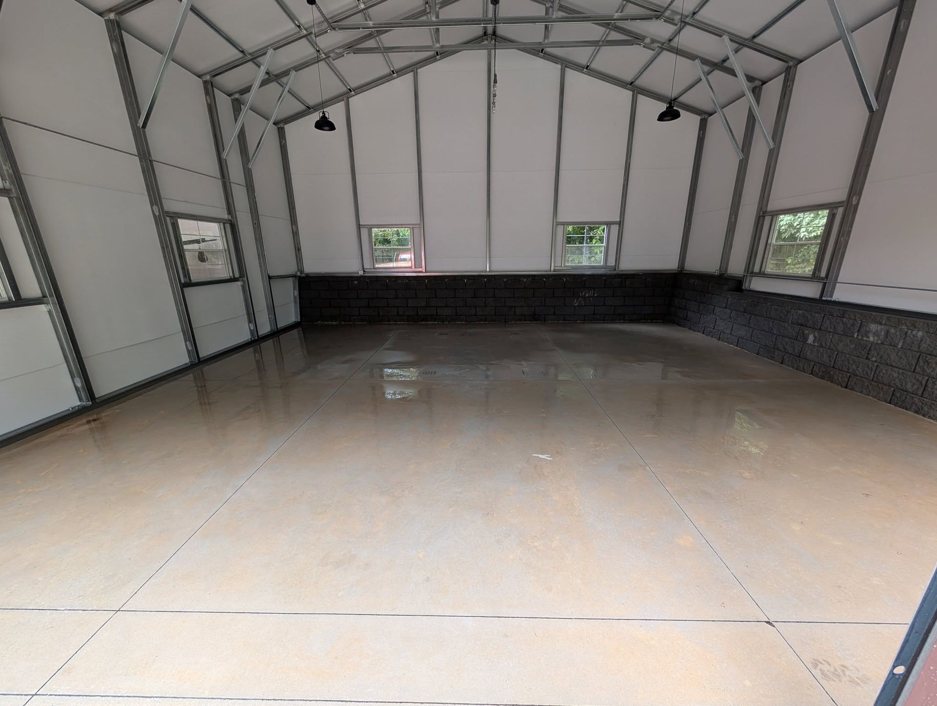 Interior of a large, empty metal building with a smooth, light brown floor and white walls.