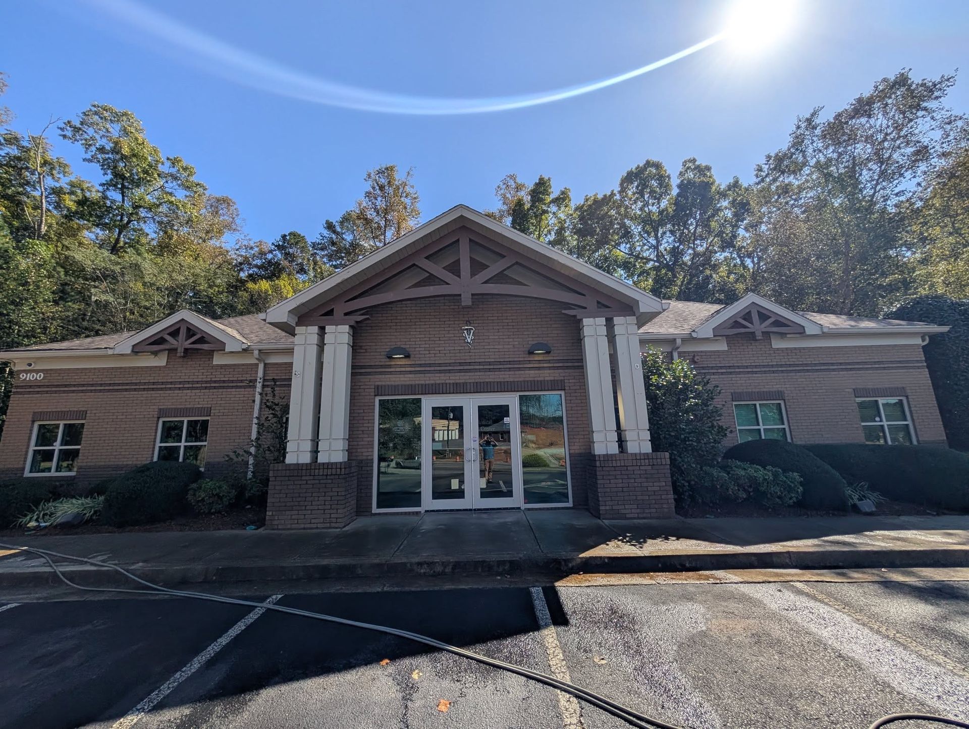 Brick building with glass doors, white columns, and a gabled entrance under a bright sky.