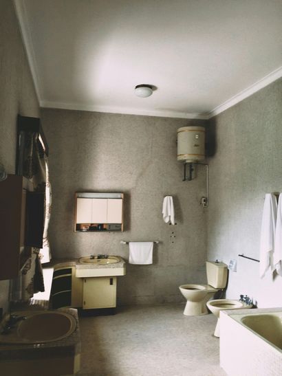 Bathroom with light fixtures, beige tiles, toilet, sink, and water heater on a gray tiled wall.
