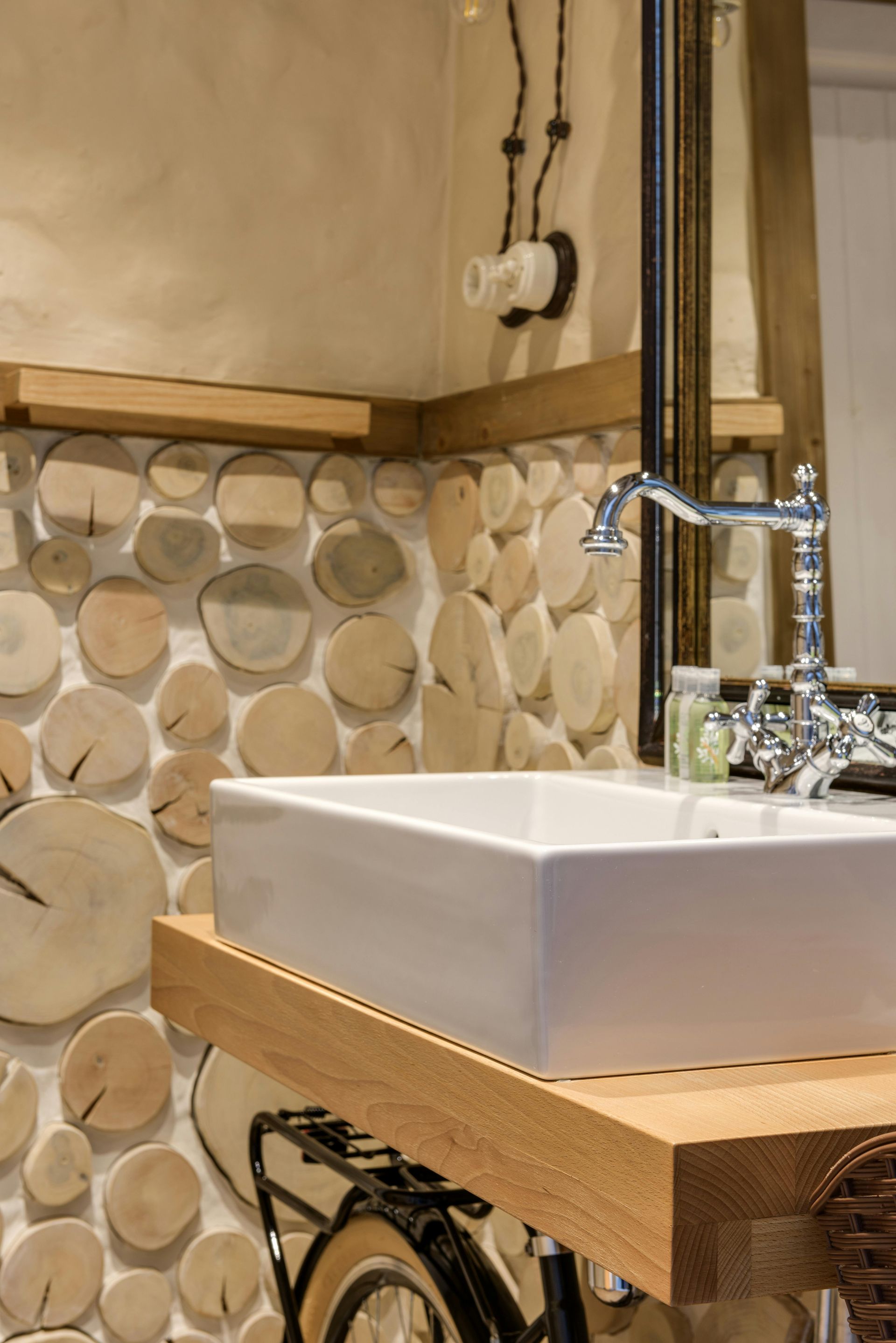 Bathroom with a white rectangular sink, wooden shelf, and a wall decorated with wooden discs.