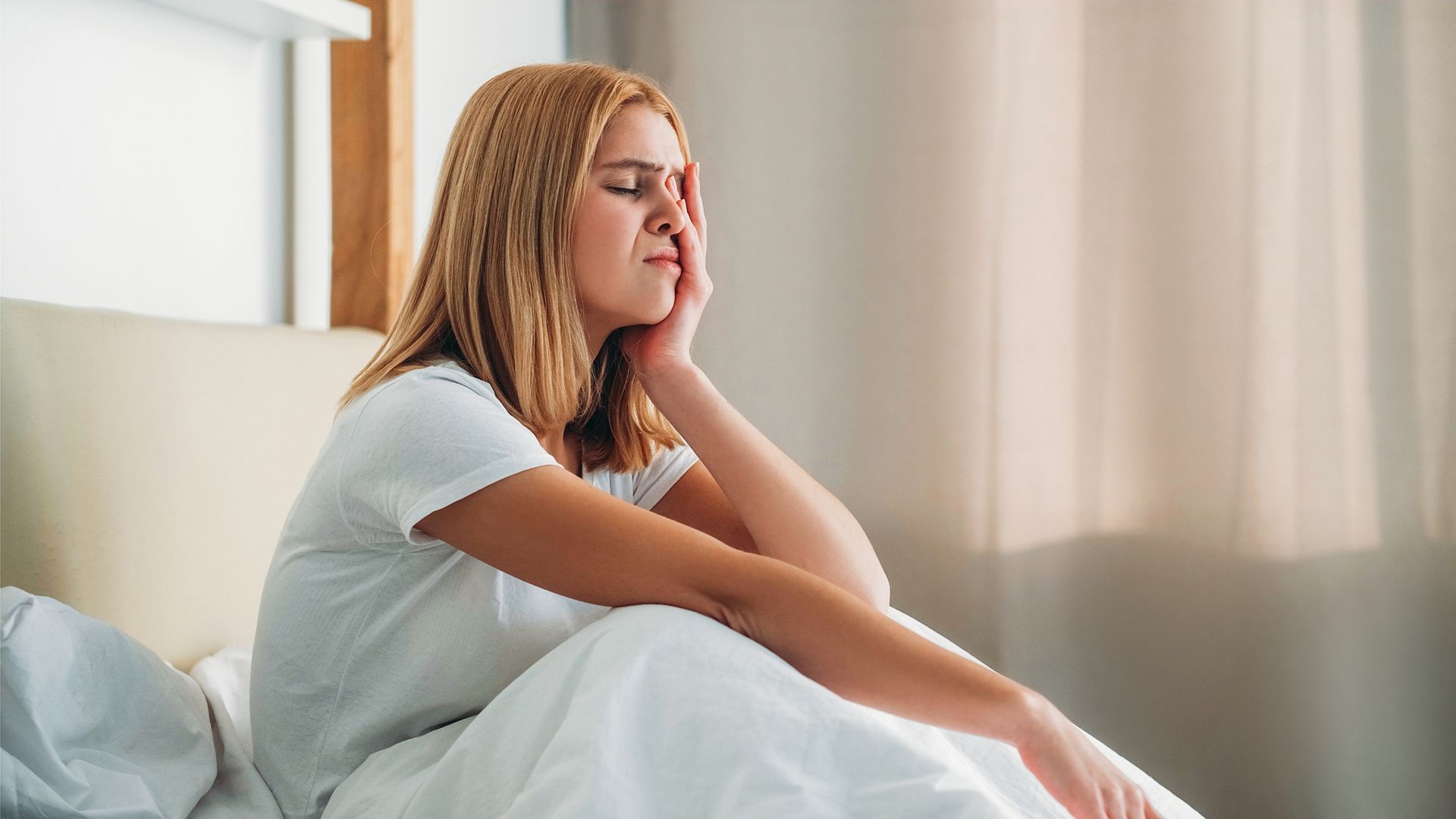 A woman is sitting on a bed with her hand on her face.