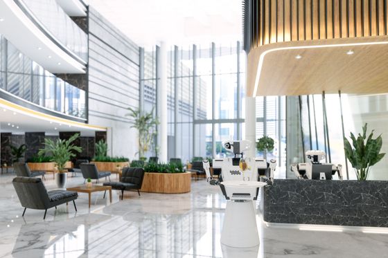 A large lobby of a modern office building with a reception desk , chairs , tables and plants.